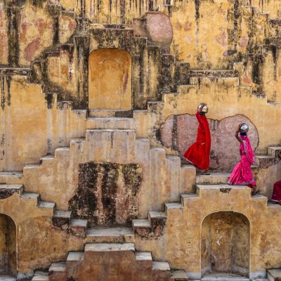 Indian women carrying water from stepwell near Jaipur, Rajasthan, India. Women and children often walk long distances to bring back jugs of water that they carry on their head. 
Stepwells are wells in which the water may be reached by descending a set of steps.